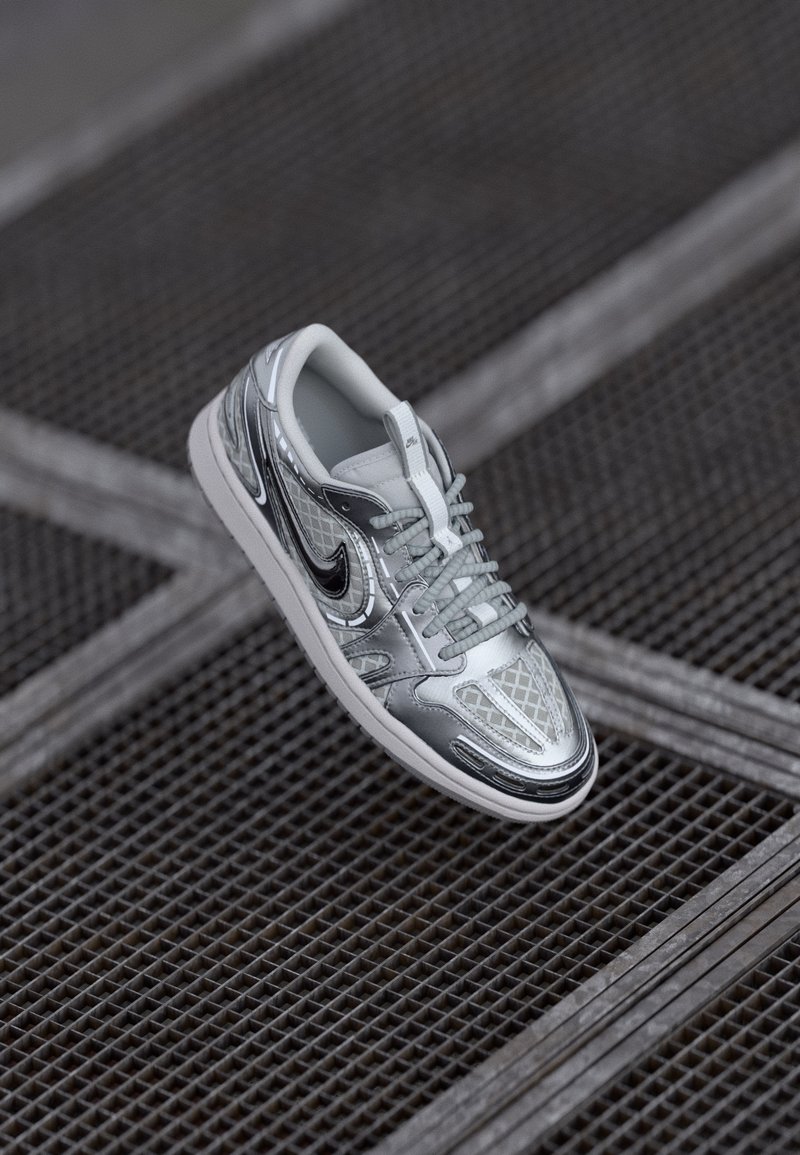 Sneaker argento con una tomaia sintetica a fantasia, accenti in mesh e logo swoosh nero. Presenta lacci e una suola in gomma bianca.