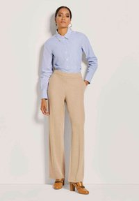 Blau gestreiftes Hemd mit Kragen, kombiniert mit beigen weit geschnittenen Hosen. Das Model trägt orangefarbene High Heels mit Kettenakzenten.