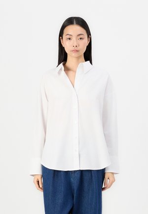 Hvit skjorte med knapper laget av lett stoff, med krage og lange ermer i en avslappet passform, kombinert med løse blå jeans.
