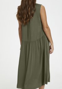 Robe sans manches vert olive en tissu doux, avec un corsage ajusté et une jupe froncée. Présente une légère évasement à l'ourlet.