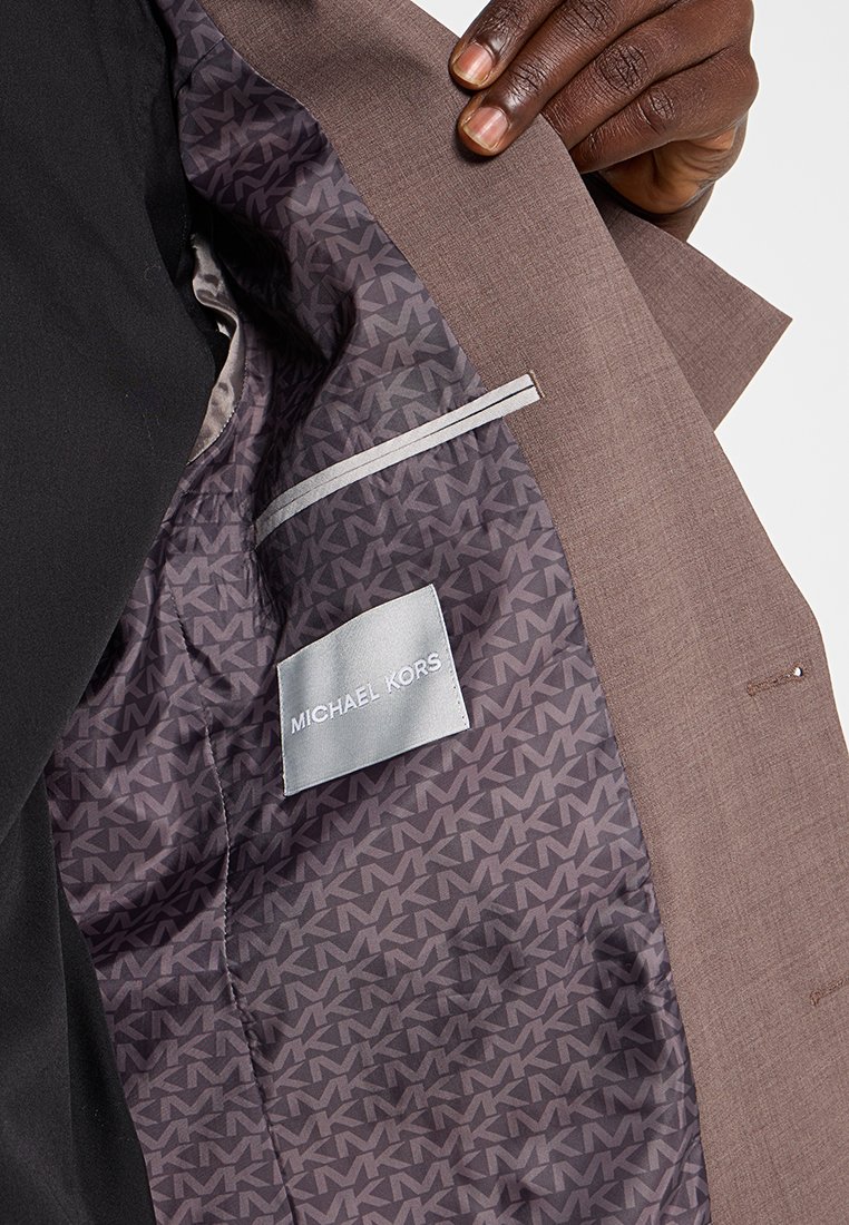Interno di giacca elegante marrone con fodera a motivo grigio scuro e il logo "MICHAEL KORS", e un'etichetta grigia chiara.