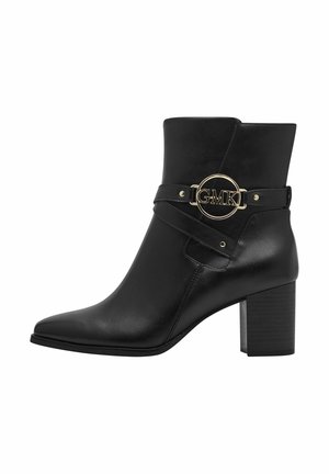Black leather ankle boot with a pointed toe, wide block heel, and gold-tone GMK logo detail on a strap around the ankle. Smooth texture.