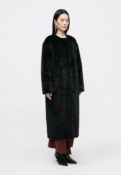 Crni kaput od umjetnog krzna s okruglim izrezom i dugim rukavima, s prednjim zatvaranjem. Glatka tekstura i dugi oblik.