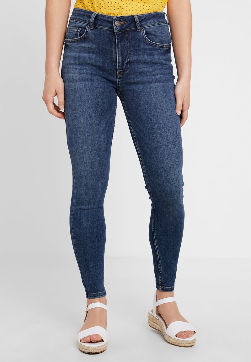 Smala jeans i denim, med en mörkblå färg, framfickor och hög midja. Matchas med vita espadriller.