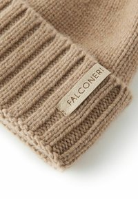Tan stickad mössa med ribbat mönster. Har en tygskylt märkt "FALCONERI" fäst vid muddarna. Mjuk textur.