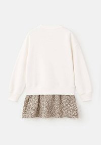 Weißer Pullover mit Rundhalsausschnitt und langen Ärmeln, versehen mit einem gestuften Rock aus einem beigen Stoff mit einem Leopardenmuster am Saum.