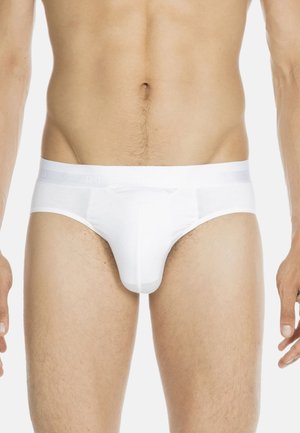 Mannelijke torso in een eenvoudige witte onderbroek, zichtbaar vanaf de taille, heupen en bovenbenen op een neutrale achtergrond.