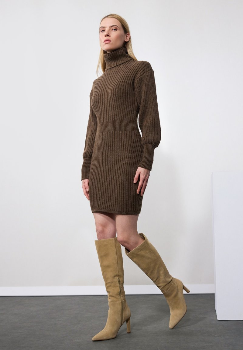 Robe en tricot côtelé marron avec un col montant et des manches longues, associée à des bottes à talons en suède beige montantes jusqu'au genou. Silhouette simple et ajustée.