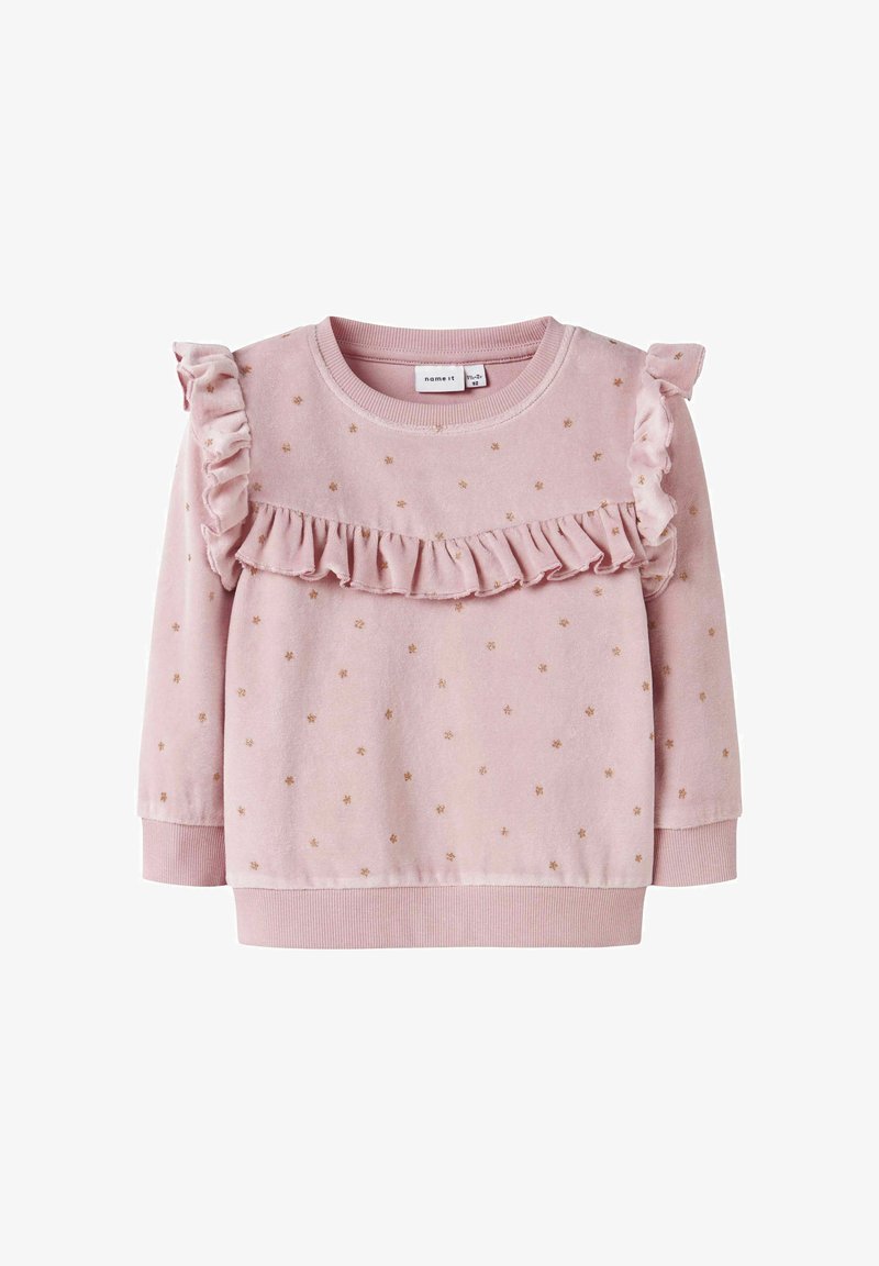 Sudadera de color rosa claro con puntos dorados, detalles con volantes en los hombros y un volante horizontal en el pecho. Puños y dobladillo acanalados.