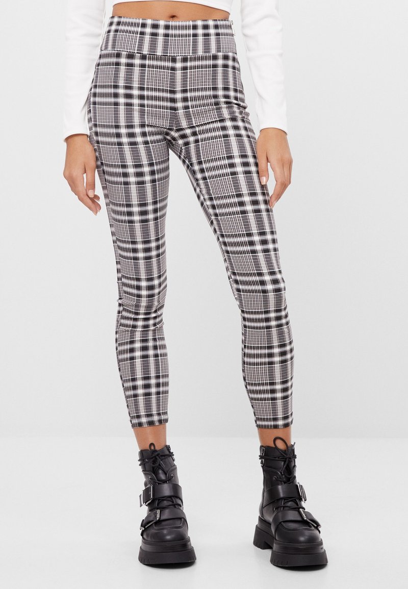 Czarno-białe legginsy w kratę z wysokim stanem, dopasowanym krojem i gładką fakturą. Noszone z masywnymi czarnymi botkami za kostkę.