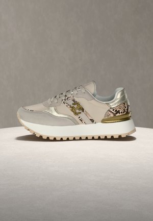 Baskets beiges avec du daim beige et des accents à motif serpent, des détails dorés, une semelle blanche épaisse et une semelle extérieure beige, présentées de profil sur une surface claire.