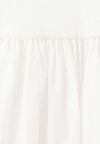 Gros plan d'un tissu blanc avec une couture froncée reliant la section supérieure lisse à la section inférieure délicatement plissée.