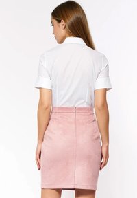 Biała bluzka z krótkim rękawem i kołnierzykiem, zestawiona z różową ołówkową spódnicą zamszową z tylnym suwakiem i wycięciem na środku.