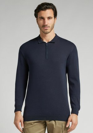 Marineblauw polo-shirt met lange mouwen en een ritssluiting bij de kraag, gemaakt van een fijne brei-stof. Heeft ribgebreide manchetten en een rechte zoom.