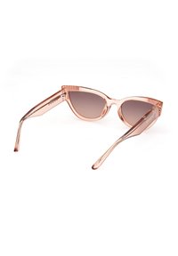 Gafas de sol de forma de ojo de gato en color rosa claro, con lentes marrones degradados, montura transparente y patillas elegantes que presentan el logo "GUESS".
