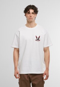 Biele bavlnené tričko s okrúhlym výstrihom a krátkymi rukávmi, so červenou grafikou krídel a oka na ľavej hrudi.