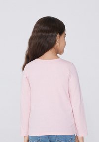 Dlouhý rukáv, světle růžové tričko vyrobené z měkké bavlny, s kulatým výstřihem a uvolněným střihem, zobrazené zezadu.