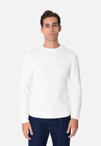Maglione bianco lavorato a maglia con un motivo a diamante testurizzato, maniche lunghe, collo rotondo e polsini e orlo a costine, indossato con jeans blu.