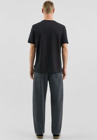 Czarna bawełniana koszulka z krótkimi rękawami, z prążkowanym, okrągłym dekoltem, zestawiona z luźnymi, ciemnoszarymi jeansami z denimu. Charakterystyczne przeszycia na jeansach.