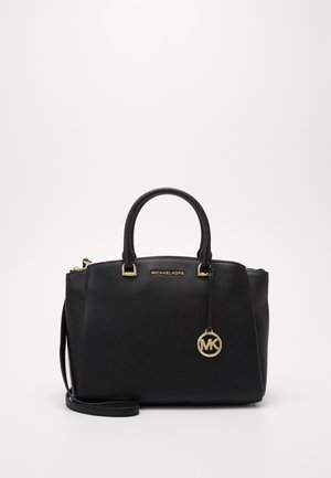 Sac à main Michael Kors en cuir noir avec deux poignées, quincaillerie dorée, breloque logo MK et une bandoulière amovible sur un fond neutre.