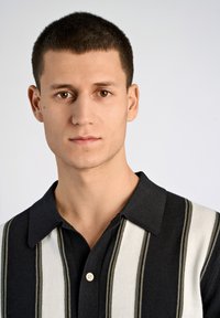 Svart- och vitrandig pikétröja med krage. Stickad textur och har en treknappslå. Enkelt, modernt design.