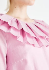 Ροζ μπλούζα με φαρδύ, βολάν κολάρο με στρώσεις πτυχών, λεία υφή και απλή στρογγυλή λαιμόκοψη.