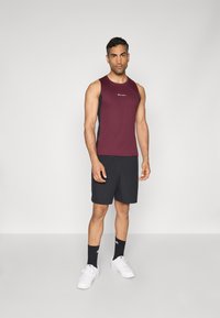 Burgundi színű, ujjatlan sporttop fekete oldalpanelek díszítésével, fekete rövidnadrággal párosítva. Fehér sportcipő és fekete zokni logóval.