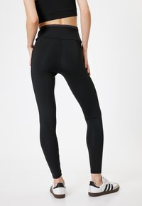 Zwarte high-waisted leggings gemaakt van rekbaar materiaal, met een gladde afwerking en een aansluitende vorm. Draagt wit sneakers.