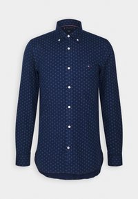 Tmavě modrá košile na zapínání s geometrickým modrým vzorem, dlouhými rukávy a zakřiveným spodním lemem. Má bílé knoflíky a malý logo na hrudi.