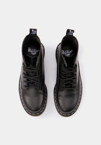 Paire de bottes Dr. Martens en cuir noir avec lacets noirs, coutures blanches autour des semelles et languettes marquées, vues de dessus sur fond blanc.