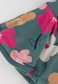 Blumengemusterter Stoff mit rosa, weißen und beigen Blumen auf einem teal-farbenen Hintergrund. Weicher Stoff, kurze Ärmel und umgeschlagener Saum.