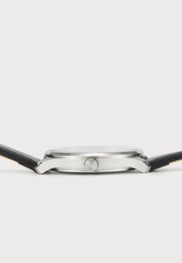 Silverfärgad rostfri stålarmband med en slät rund urtavla, svart läderrem och en strukturerad krona. Minimalistisk design utan synliga markeringar.