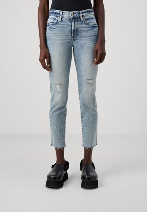 Jean court délavé bleu clair porté avec des chaussures noires à plateforme sans lacets et un haut noir, montré sur une personne debout sur un fond uni.