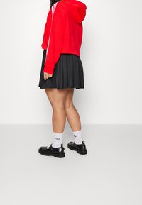 Czerwony krótki hoodie z białymi paskami, czarna plisowana spódnica, białe skarpetki z czarnym logo oraz czarne buty na solidnej podeszwie.