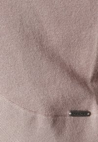 Ljust rosa, texturerat tyg med ett subtilt ribbat mönster. Inkluderar en liten metalltagg med texten "MORE & MORE" längst ner.