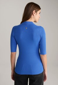 Gestreifter blauer Strickoberteil mit kurzen Ärmeln, mit einem runden Halsausschnitt und einem kleinen Logodetail auf der Rückseite. Glatte Textur.
