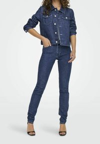 Completo giacca di jeans e jeans skinny in blu scuro. La giacca presenta chiusure con bottoni e tasche frontali. Jeans aderenti con design semplice e lunghezza alla caviglia.