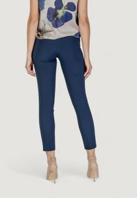 Pantaloni navy su misura con vestibilità slim, tessuto elasticizzato e taglio alla caviglia; indossati con una blusa floreale e scarpe con tacchi alti color nude.