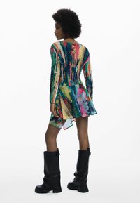 Színes, hosszú ujjú ruha aszimmetrikus szegéllyel, texturált ecsetvonás-mintával kék, rózsaszín, zöld és sárga árnyalatokban. Fekete térdig érő csizma.
