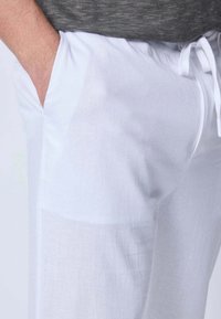 Pantalons en lin blancs avec taille à cordon de serrage, poches latérales et une texture légère et respirante. Fini lisse avec une légère translucidité.