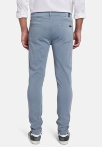 Lichtblauwe slim-fit broek met twee achterzakken. Gemaakt van een gladde stof, met een riemlus en subtiele stikseldetails.