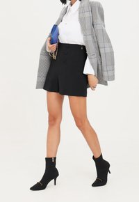 Mini gonna nera con pieghe frontali, abbinata a una camicia bianca e un blazer grigio a quadri. Presenta stivali alla caviglia neri a punta con dettagli dorati.