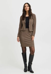 Rjav blazer s houndstooth vzorom in svinčnik krilo s črno majico, v kombinaciji z visokimi črnimi škornji, ki se odlikujejo po gladki teksturi in prilegajočem dizajnu.
