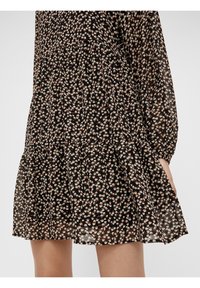 Robe noire à fleurs avec un ourlet à volants superposés, manches longues et texture transparente ornée de petits motifs floraux beiges et roses.