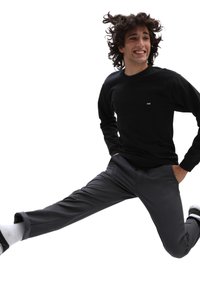 Cămașă neagră cu mâneci lungi și un mic logo, asociată cu pantaloni gri. Model în aer, având o croială lejeră, evidențiind textura și designul materialului.