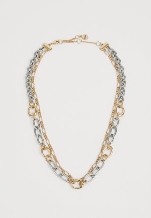 Dubbellaagse ketting met afwisselend gouden en zilveren schakels en een klein rond label nabij de sluiting.
