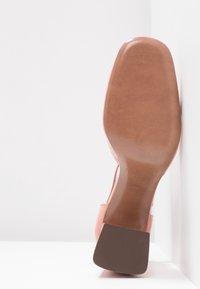 Vue de la semelle d'une chaussure habillée pour femme de couleur camel avec un talon carré, taille 38, positionnée verticalement sur fond blanc.