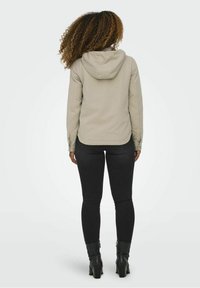 Beige hooded jacket with a smooth texture, front zip closure, and long sleeves, paired with black fitted pants and ankle boots.