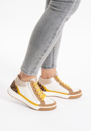 Person wearing gray jeans and white high-top sneakers with yellow laces and leopard print accents, standing on a white floor.