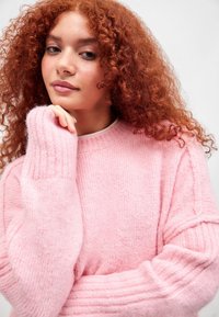 Helles, rosa Strickpullover mit Rippmuster, oversized Schnitt und weiten Ärmeln, ausgestattet mit einer weichen Textur und einem Rundhalsausschnitt.
